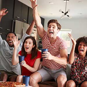 Quatre jeunes amis adultes regardant les sports à la télé et qui célèbrent.