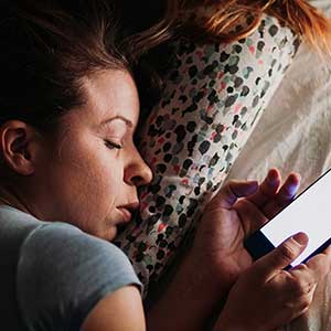 Jeune femme au lit utilisant un téléphone intelligent le soir.
